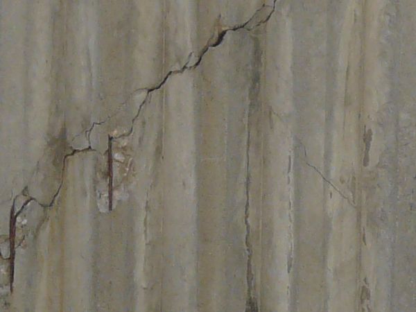 Concrete fence texture molded with a pattern of circles above vertical recessions, with large cracks and stains. The fence appears to be crumbling around the edges.